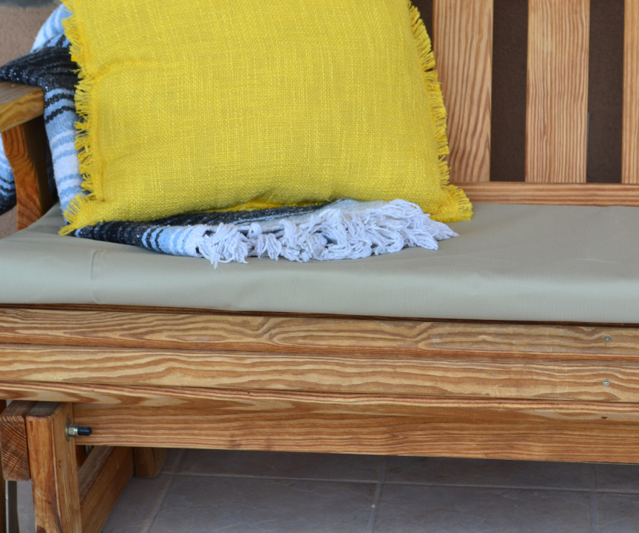 close up image of a weathered wooden bench and a beige cushion with a yellow pillow and blue tassel blanket